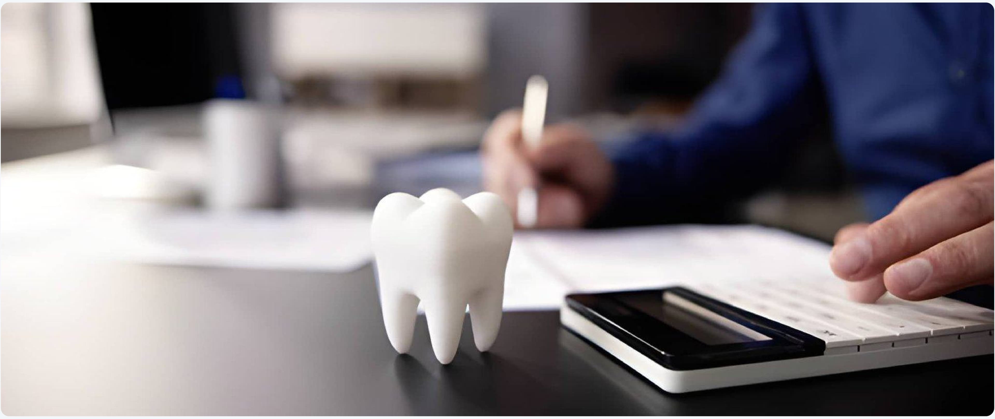 Tooth model on a desk beside financial paperwork and a calculator